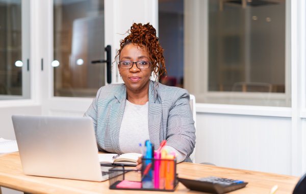 African mature black woman sitting at desk with laptop wearing glasses at the office.