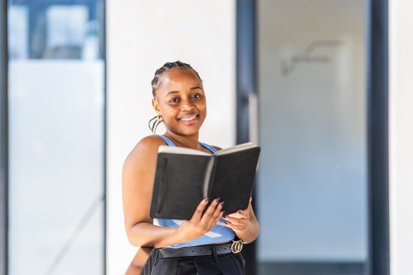 Attractive young black woman holding a writing pad smiling looking at the camera at the office.