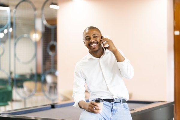 Black man smiling and talking on his cellphone by a pool table at work
