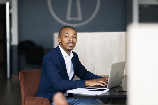 Black business man looking at the camera while working on his laptop