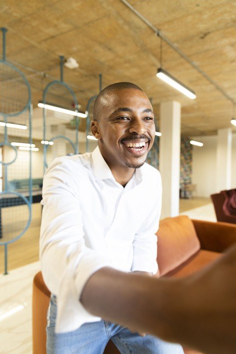 Black business man wearing jeans approaching to shake hands with a client at work while smiling