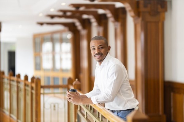 Black business man leaning over a railing at the office and smiling
