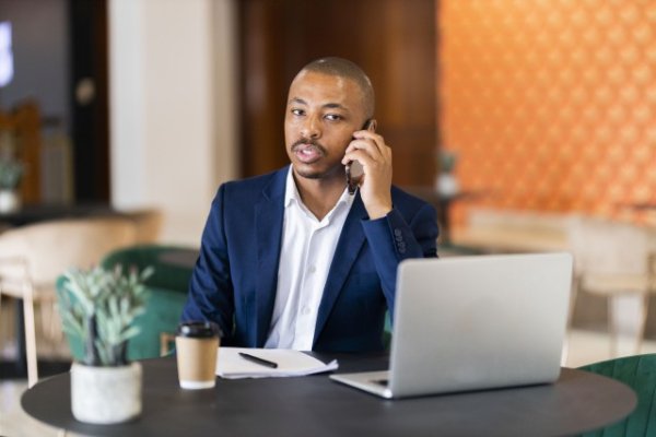 Black business man on a phone call and working on his laptop at a coffee shop