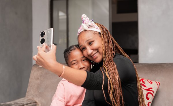 Black family taking a photo in the lounge, mother and daughter embrace on the couch.