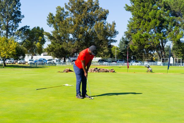 Black golfer wearing a red golf shirt putting on the green for a birdie