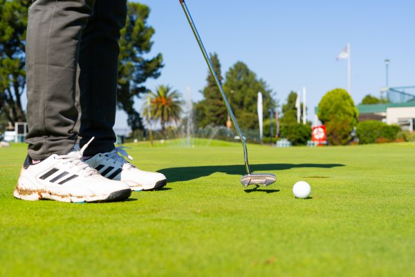 Black golfer wearing Adidas golf shoes putting on the green