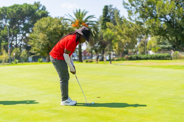 Black male golfer wearing a red golf shirt putting a golf ball with Adidas shoes