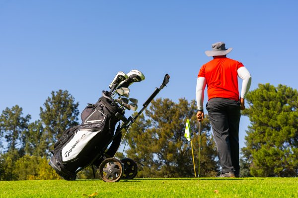 Black man wearing a red golf shirt with a Taylormade bag about to putt