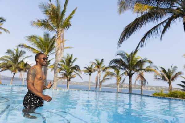 Black man with tattoos in a swimming pool wearing sunglasses.
