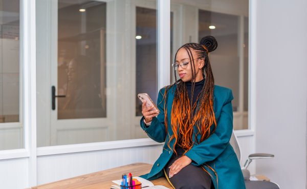 Black woman smiling at phone at the office with braids.