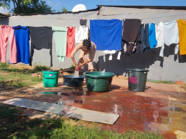 Black woman washing clothes outside her yard.