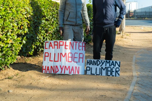 Jobless men with carpenter, plumber and handyman signs.