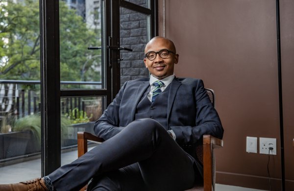 Black businessman sitting on a chair smiling with a suit on.