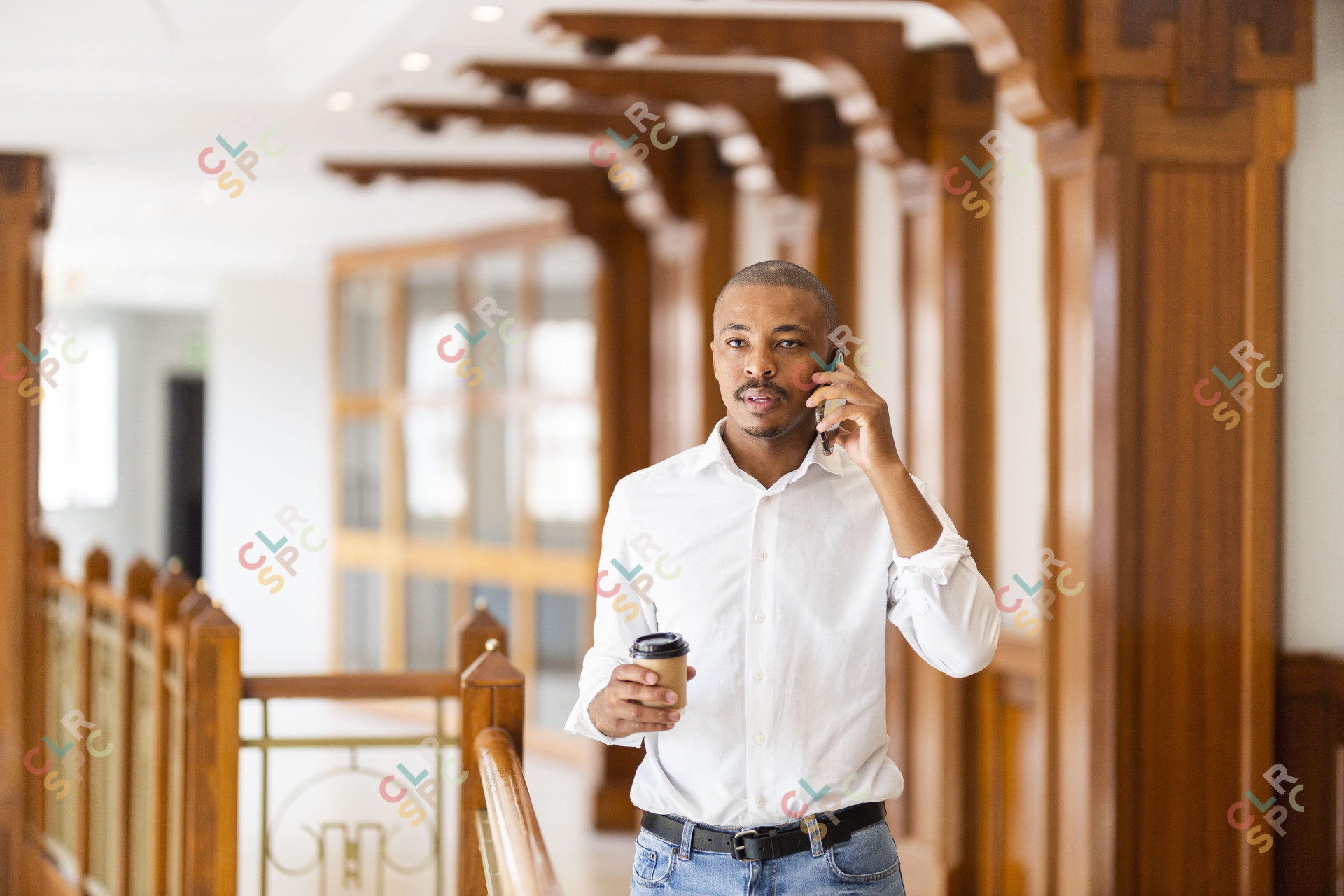 Black business man at work holding coffee and talking on the phone