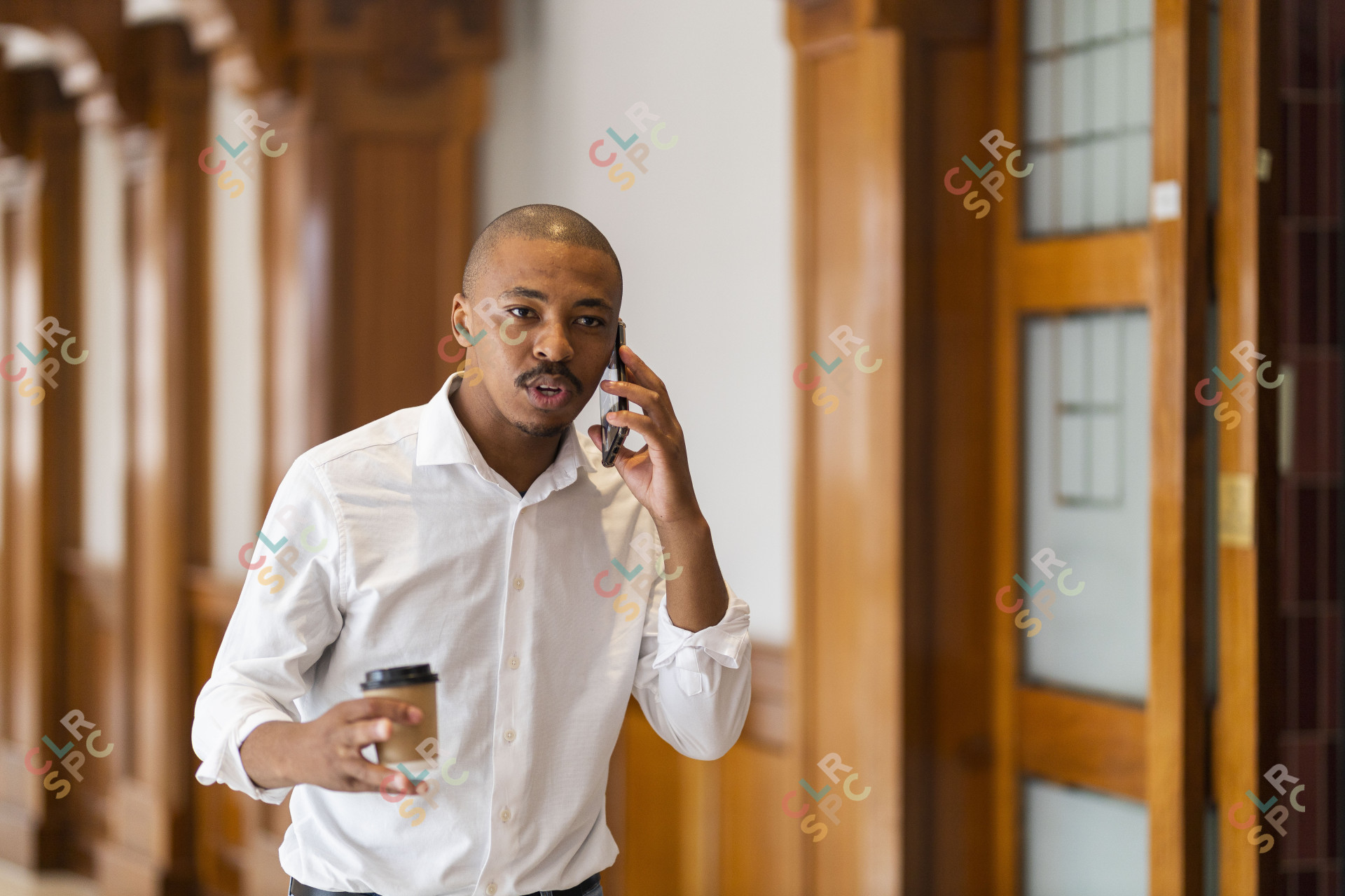 Black business man at work holding coffee and talking on the phone