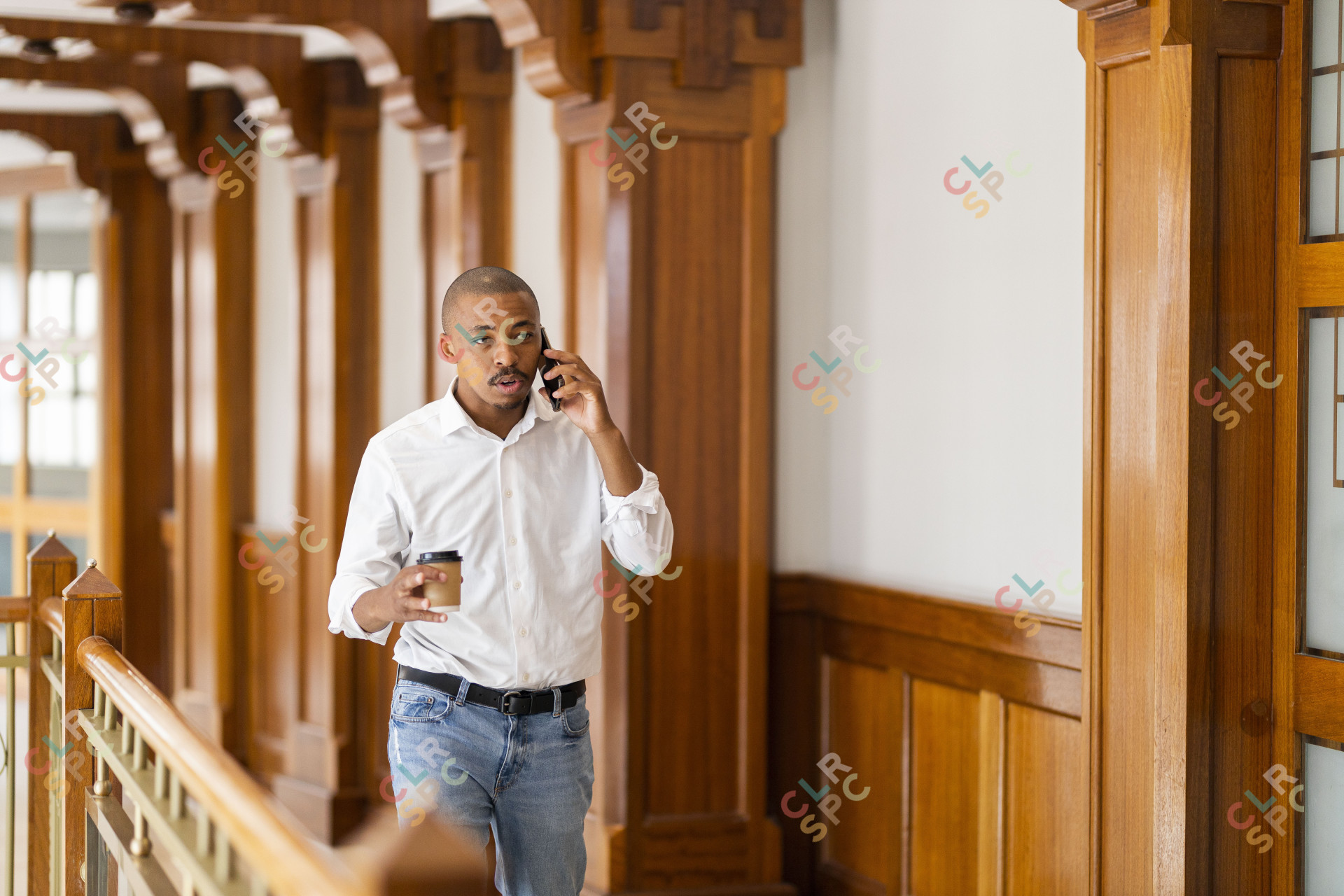 Black business man at work holding coffee and talking on the phone