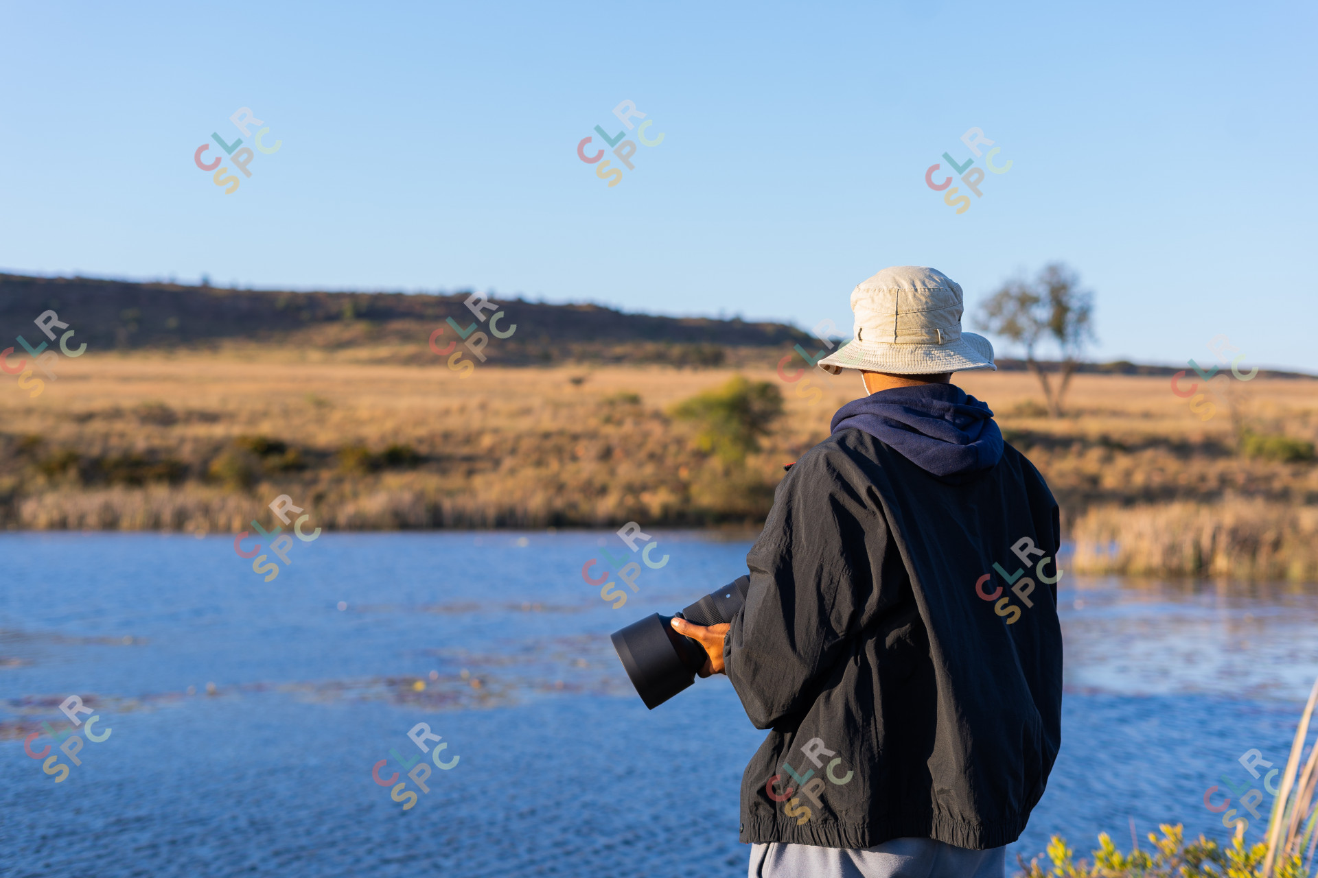 Black man standing by a river holding a camera.