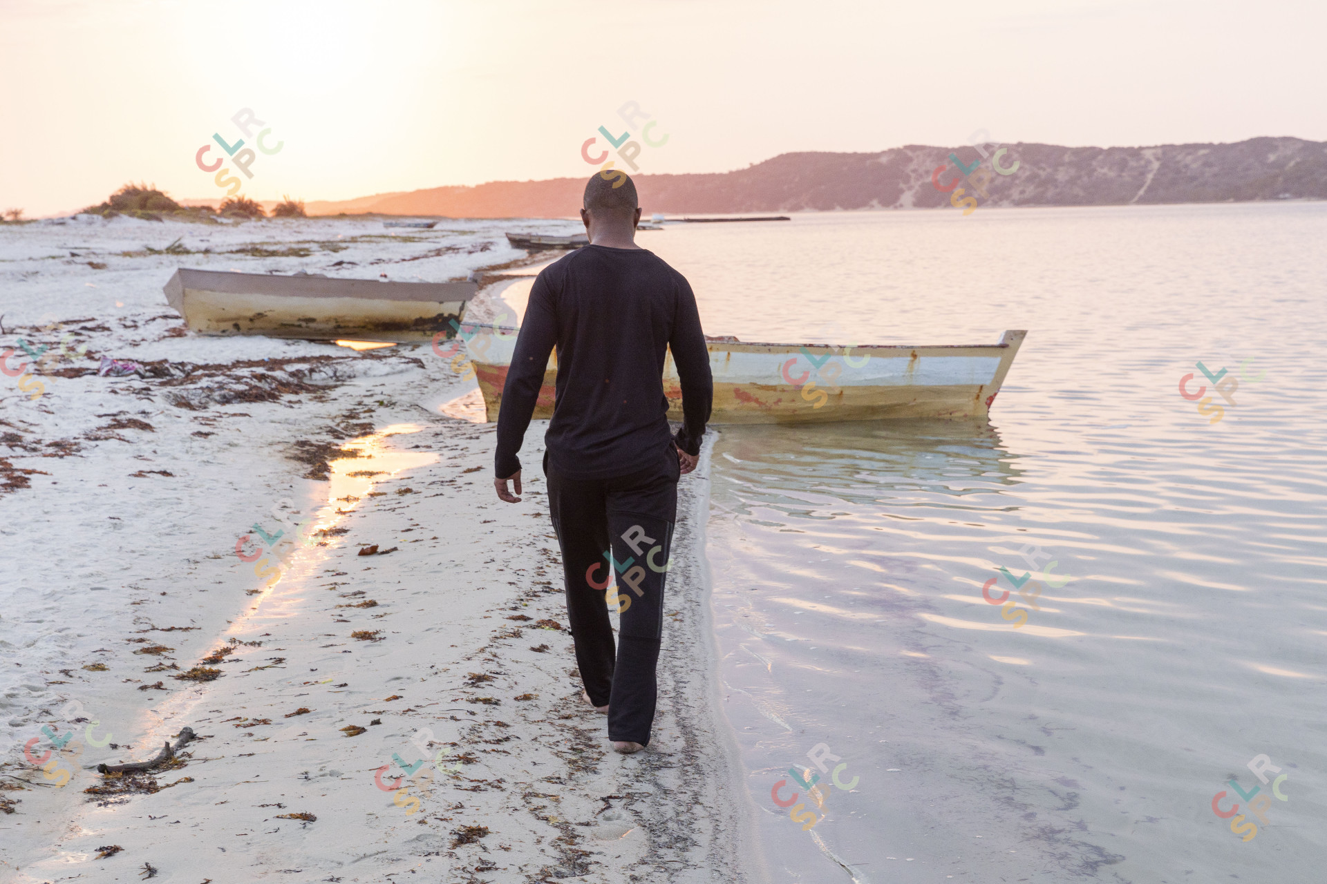 Black man walking near a lagoon with boats.