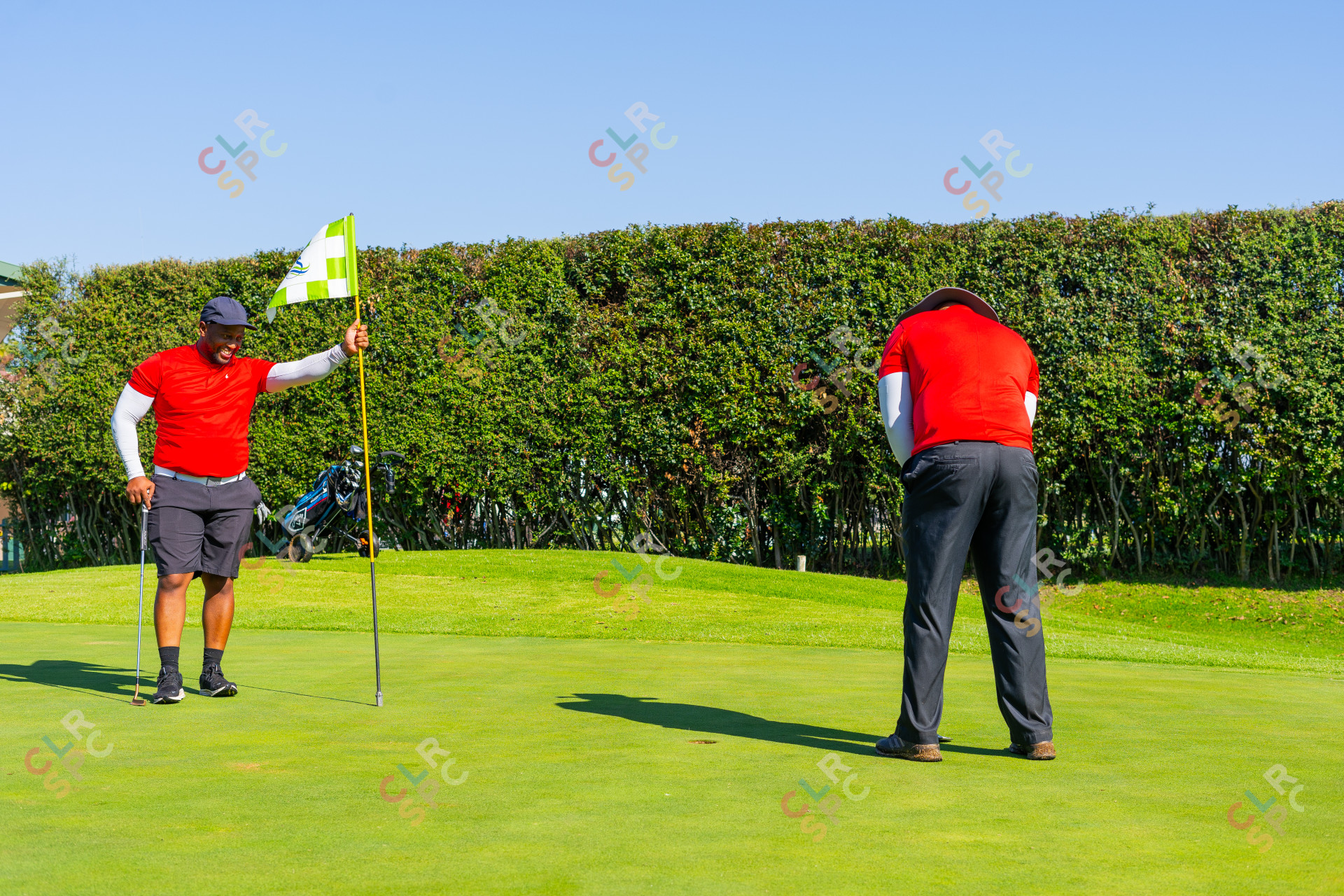 Two black men wearing a red golf shirts putting