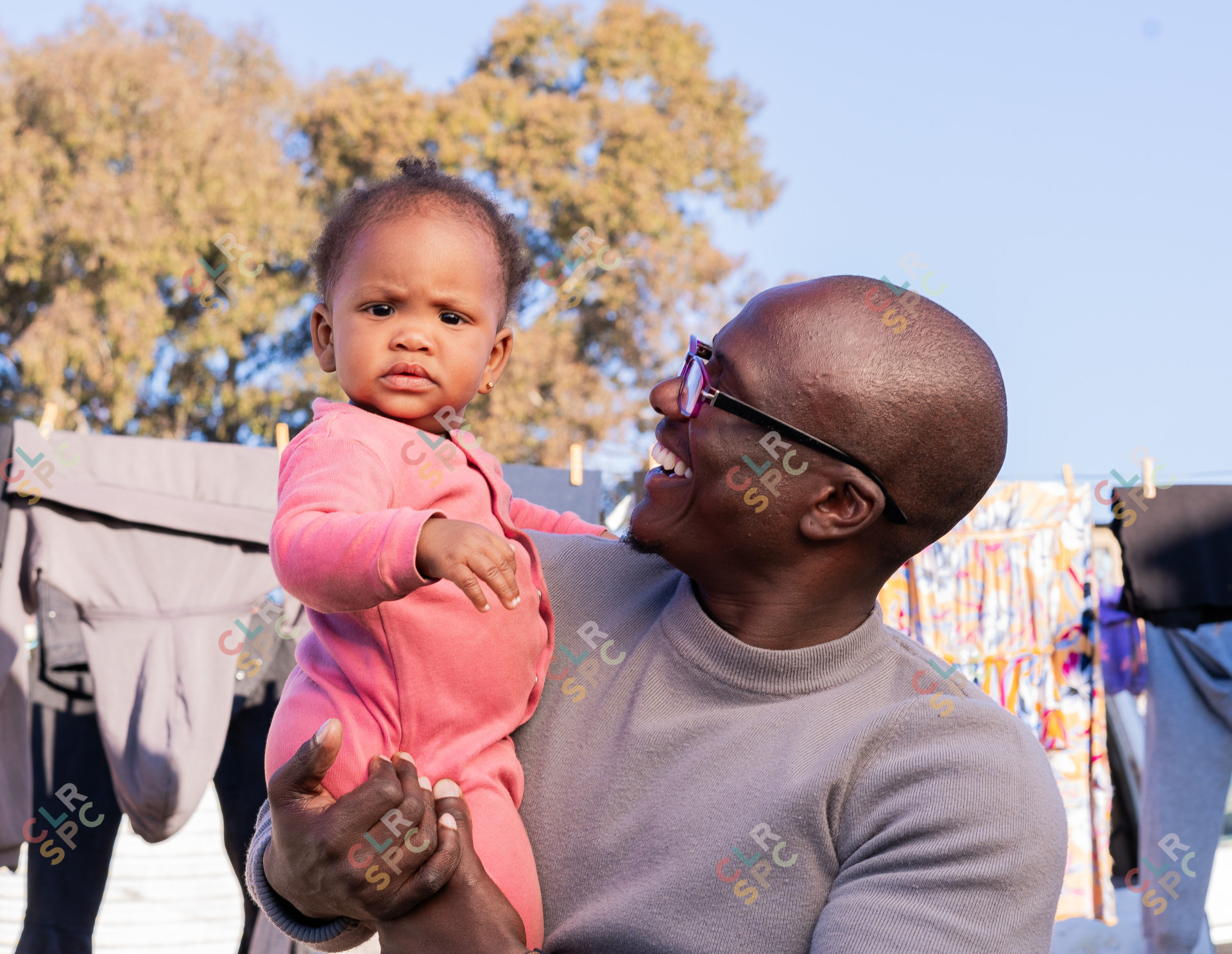 Black father smiling with daughter wearing pink and clothes hanging in the background