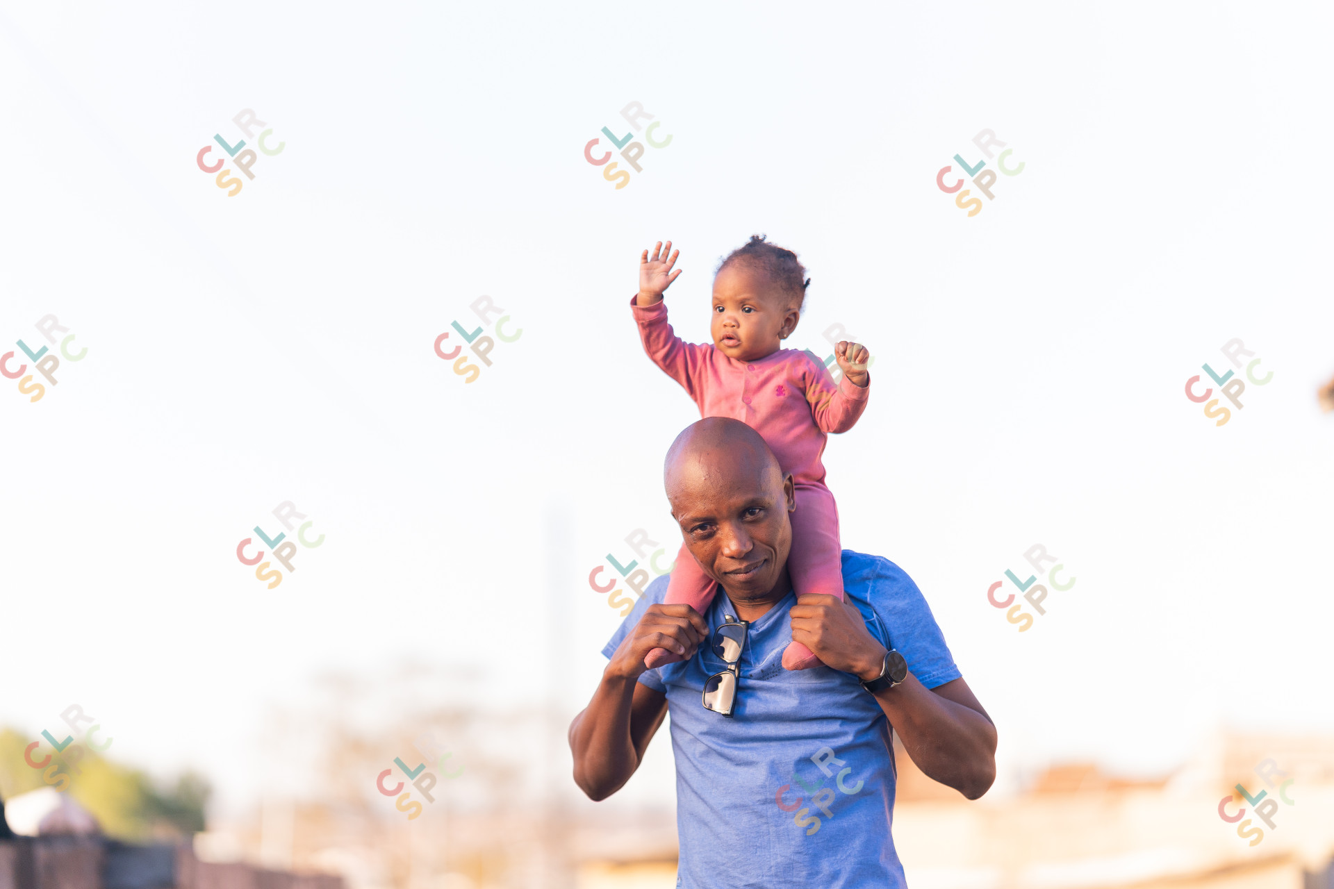 Black father carrying daughter on shoulders outside having fun wearing a blue shirt and watch.