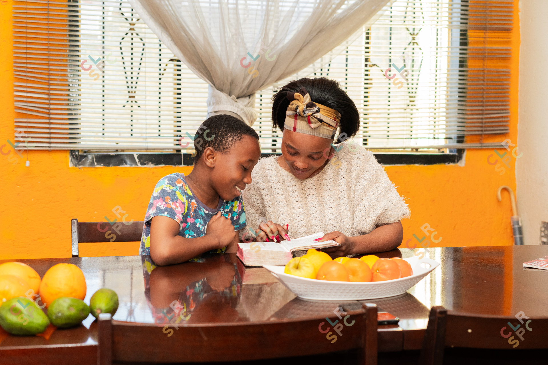 Mother and son reading the bible at home with fruits in the foreground.