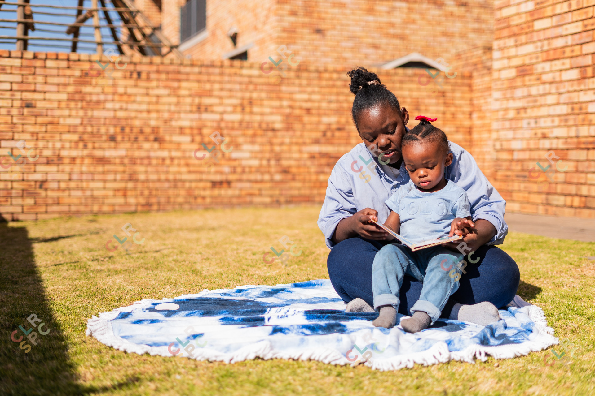 Mother and daughter reading a book on a sunny day outdoors on a blue blanket.
