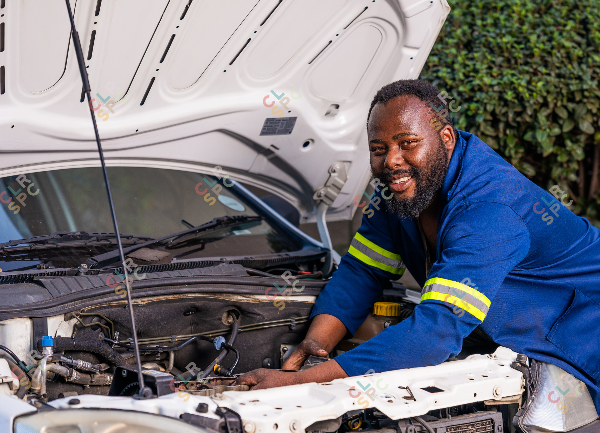 Auto car repair service. Black mechanic examining car engine wearing blue uniform.
