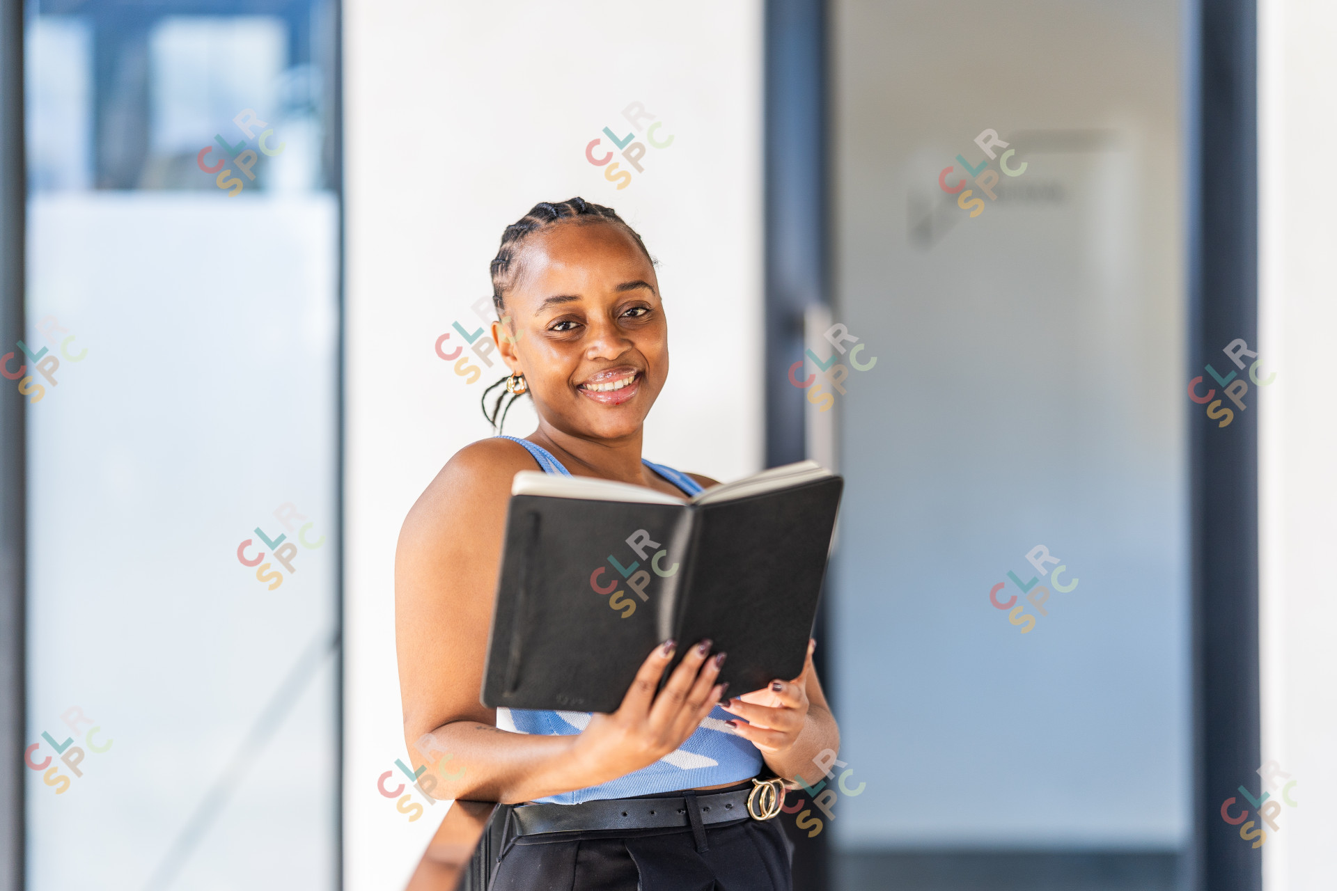 Attractive young black woman holding a writing pad smiling looking at the camera at the office.