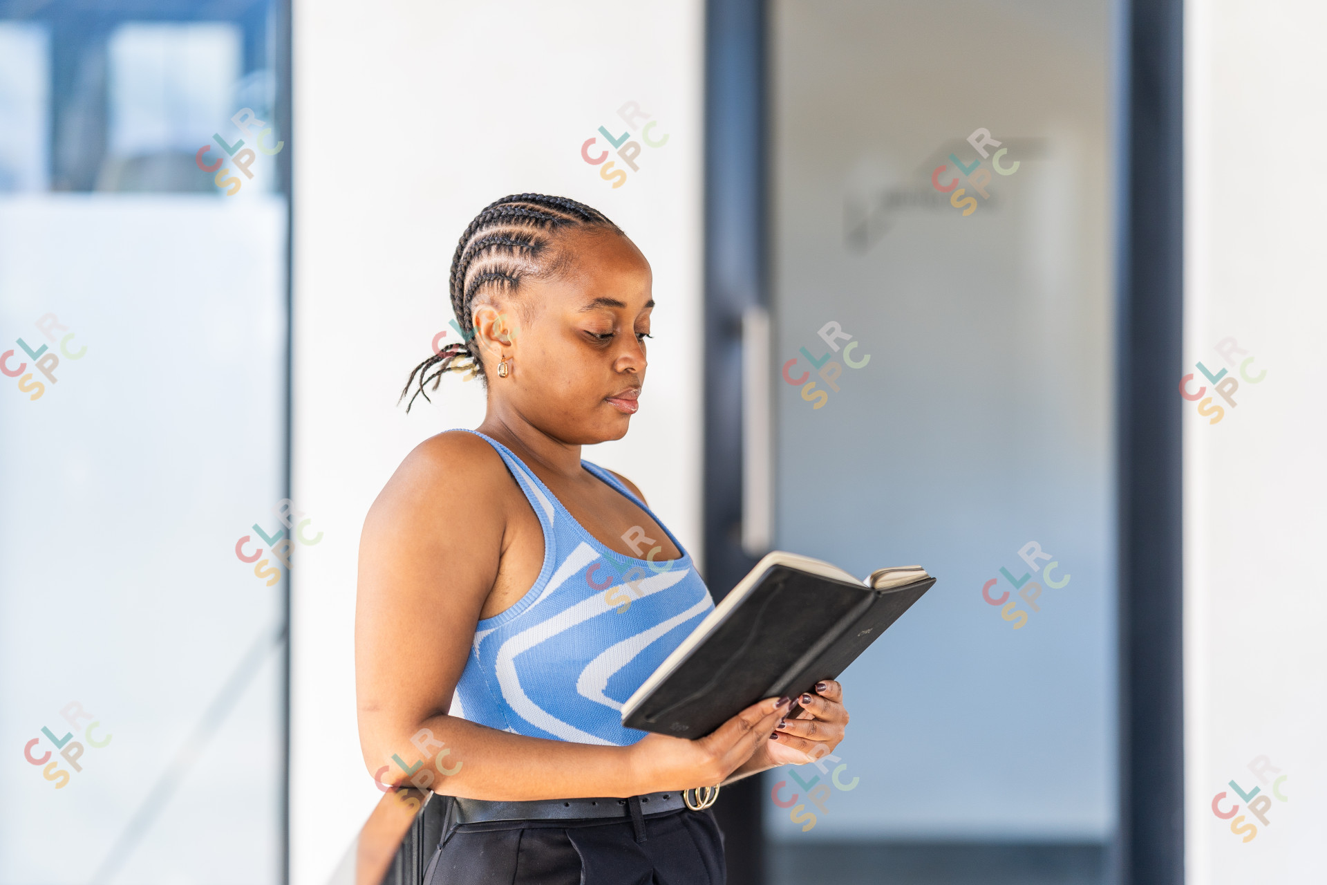Young corporate black woman with braids reading a notepad at work wearing a blue top.