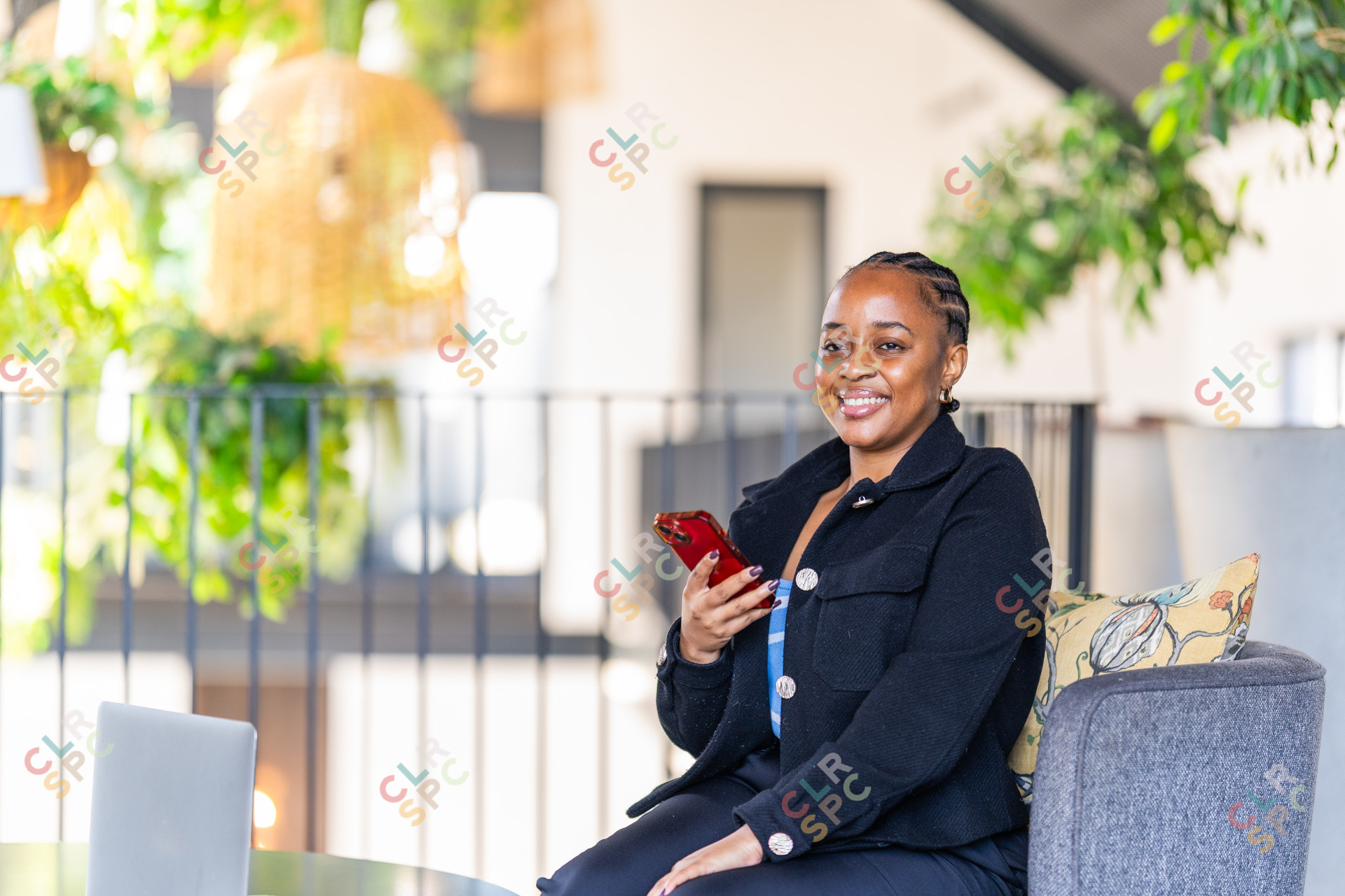Black corporate woman sitting on the couch in a co working space holding phone.
