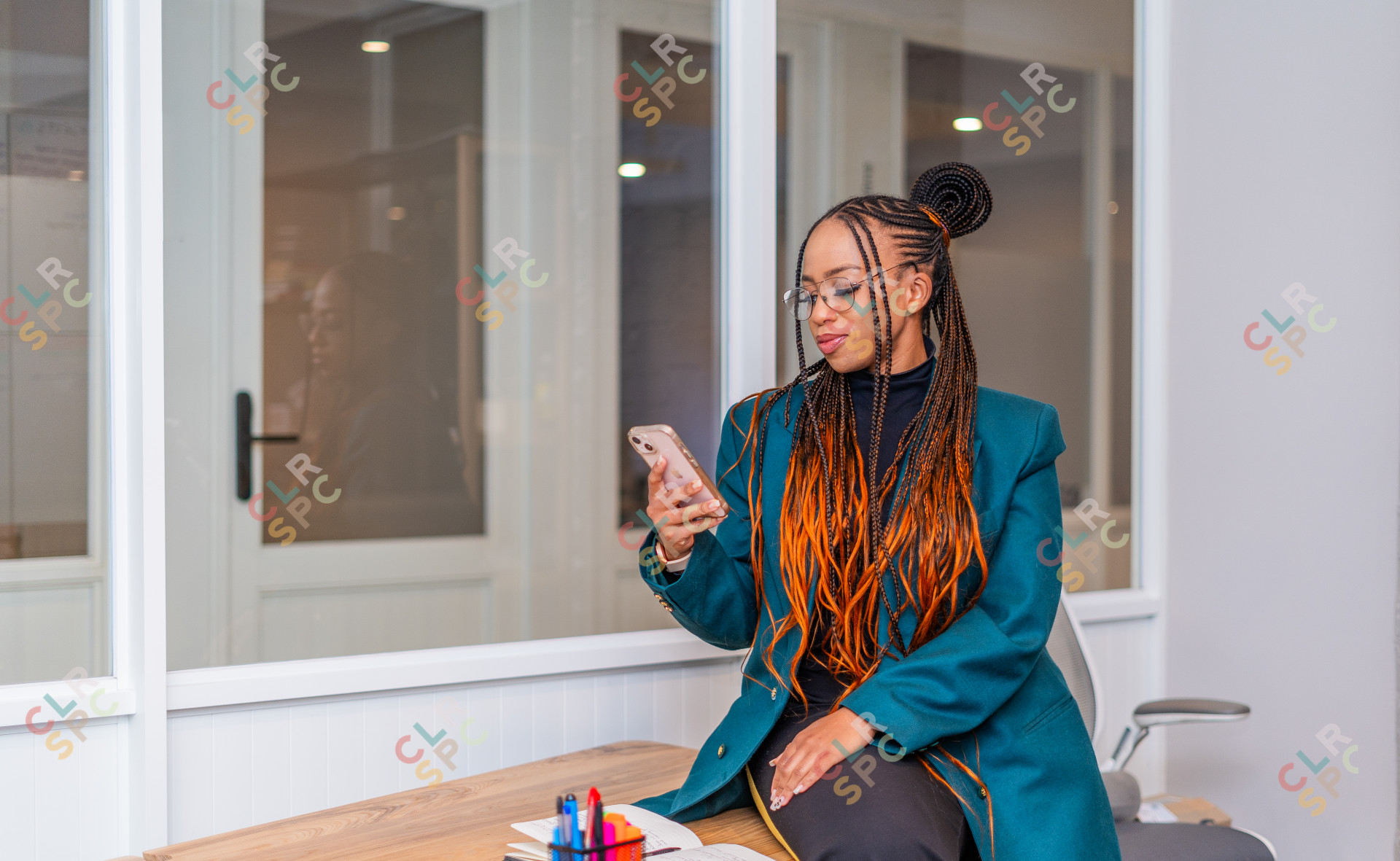 Black woman smiling at phone at the office with braids.