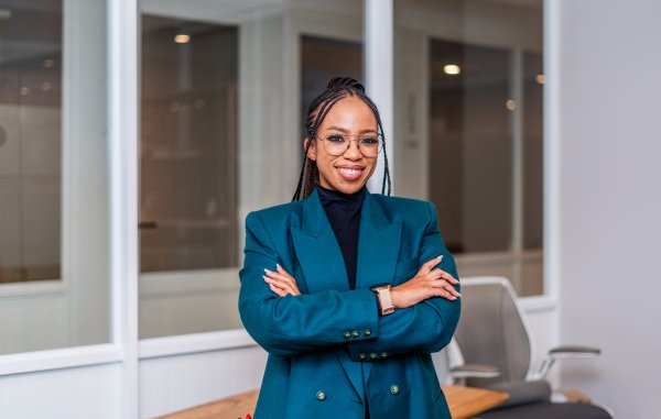 Young African business woman smiling at the office wearing a green jacket and glasses.